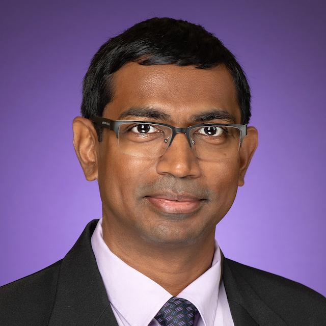 Photo of Dr. Don Galbadage in front of a purple background, wearing a button-down collared shirt, tie, and black jacket