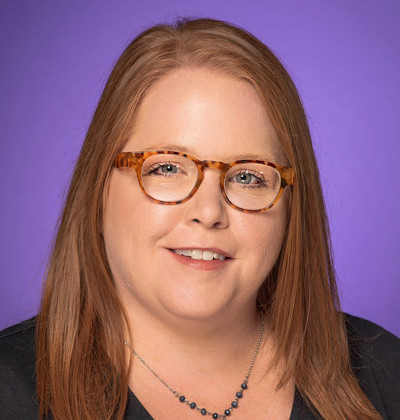 Photo of Beth Rogers, nursing professor. She is wearing a black shirt and black necklace, with tortoise shell glasses and a TCU Purple background.