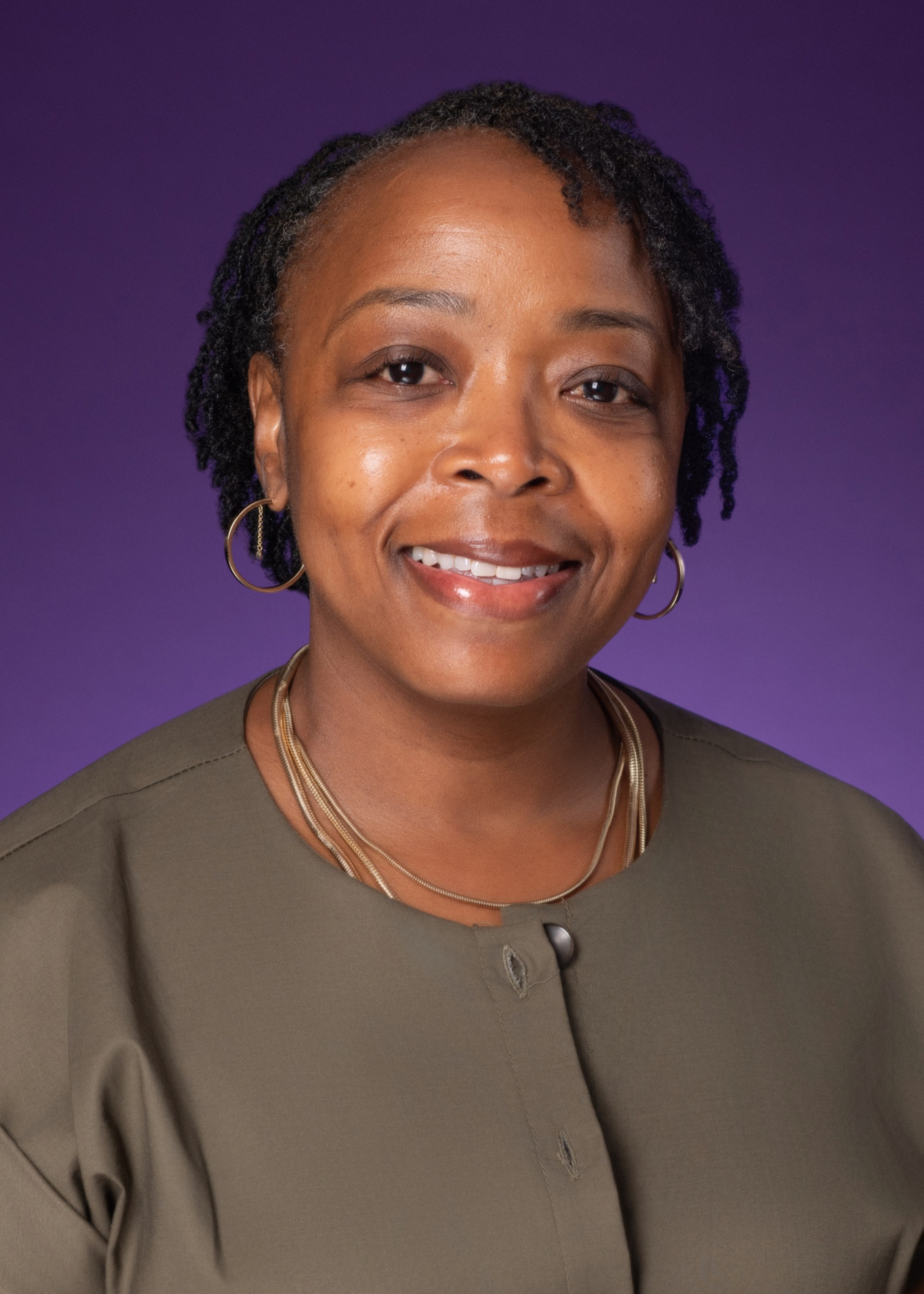 A photo of a woman smiling, wearing a bronze colored shirt with a purple background