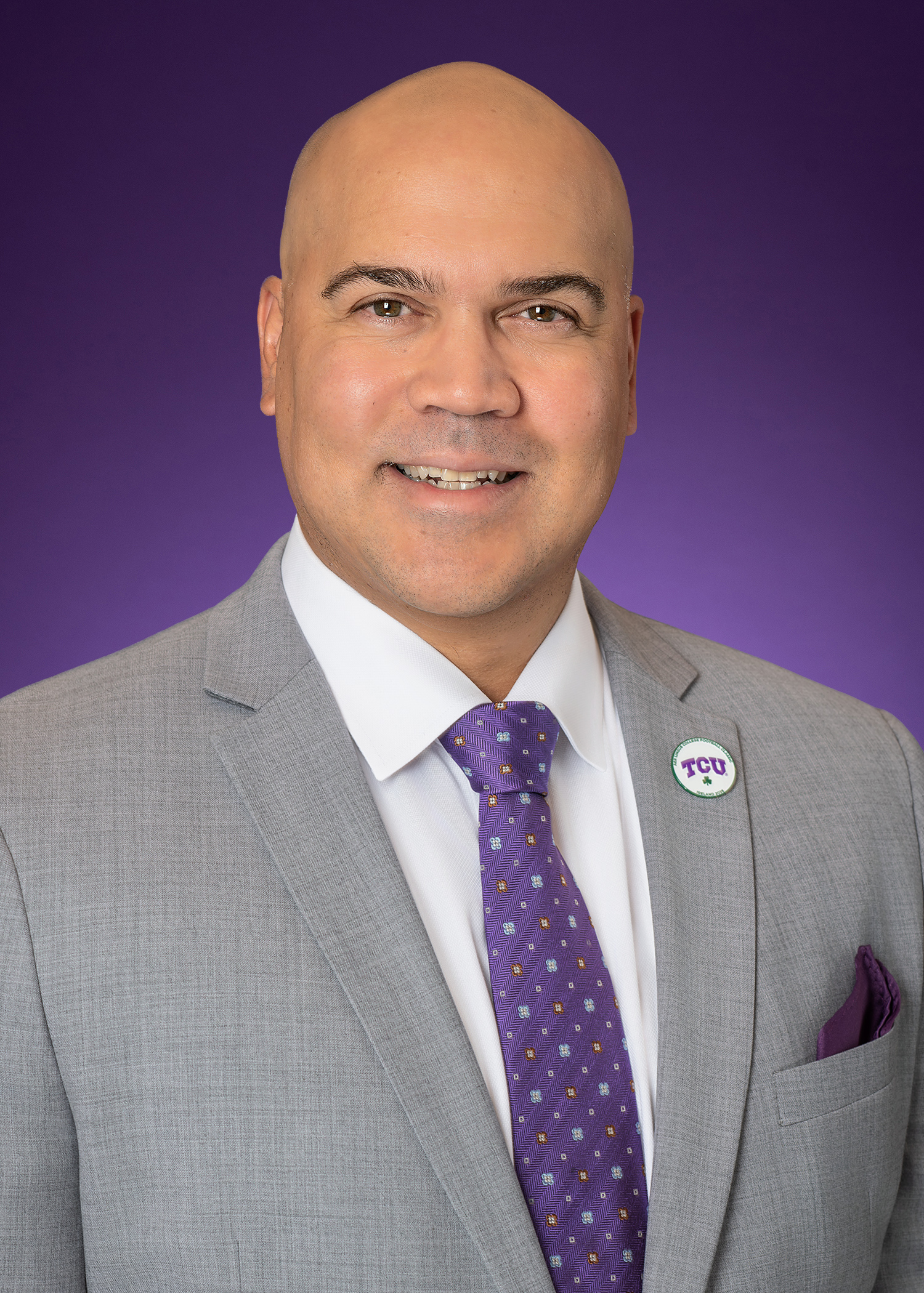 Photo of Dr. Bernard Rousseau, dean of Harris College announced in 2026. He is wearing a white button-down collared shirt with a purple tie and gray jacket, with a purple background