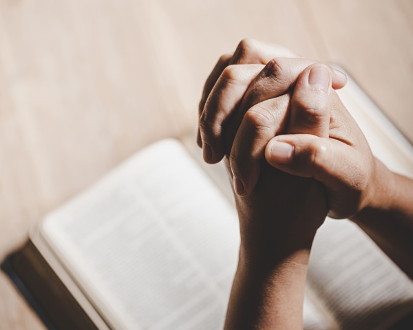 hands clasped together to pray and bible on table