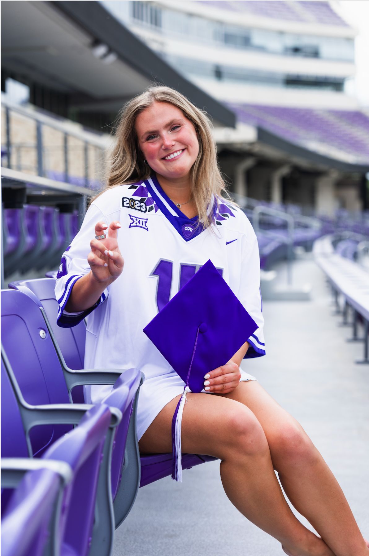Savannah Biehunko, Class of 2026, in the football stadium in a jersey, throwing up "Go Frogs" and holding a graduation cap