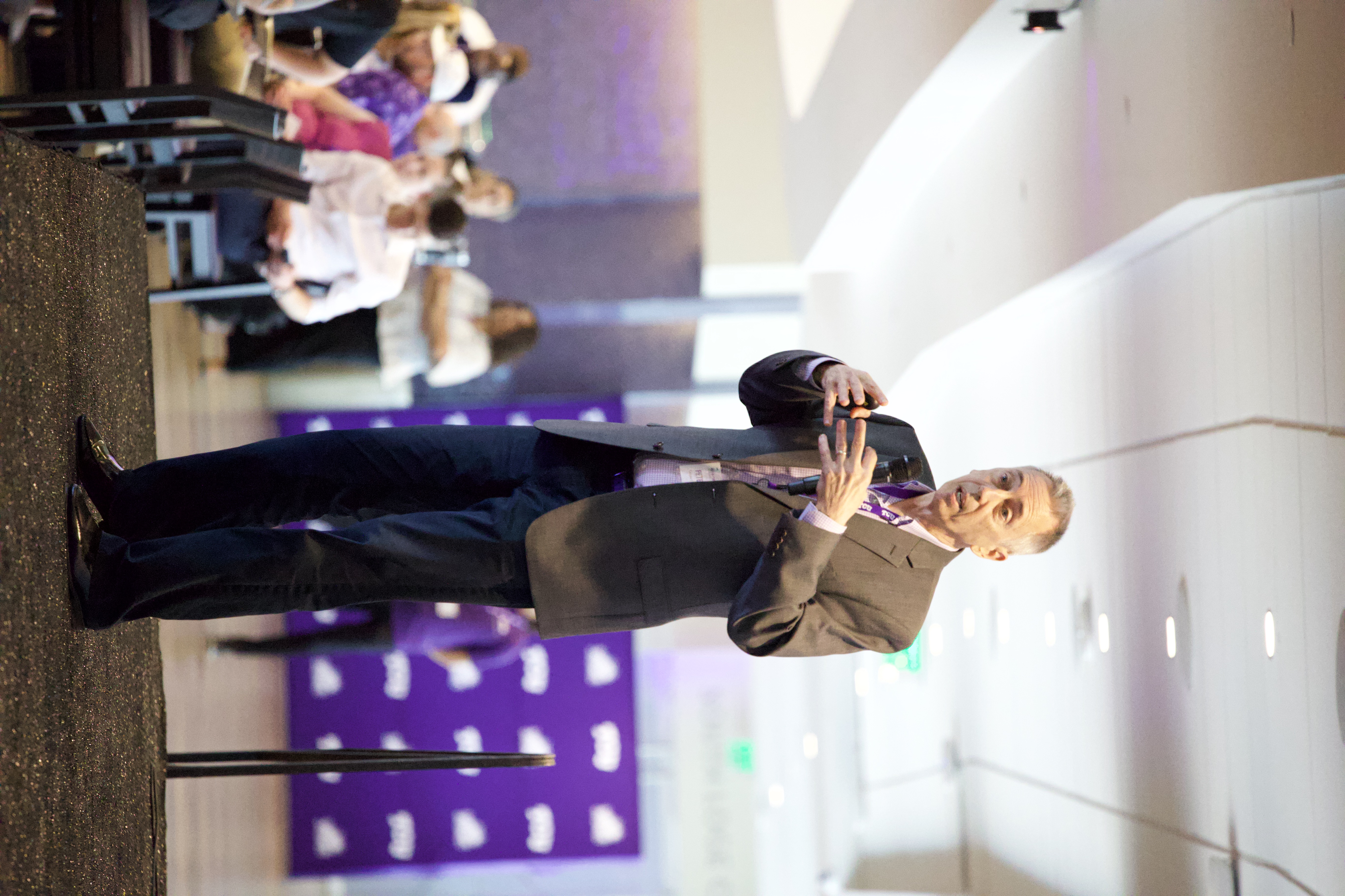 Dr. Peter Weyand on stage at the Global Human Performance Forum in June 2026, giving the keynote speech. People are seated at tables behind him, listening. 