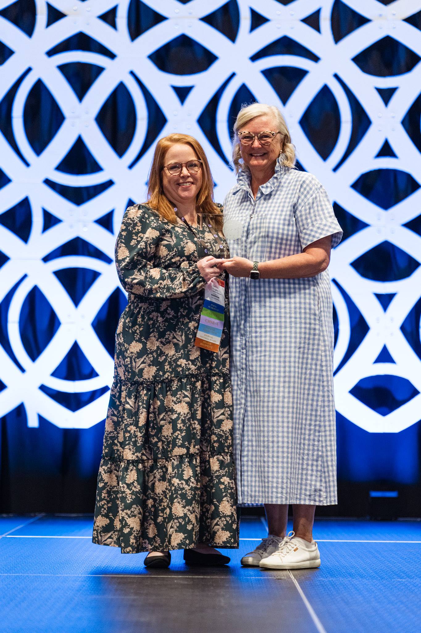 Dr. Beth Rogers, left, on stage receiving an award. Another woman stands next to her. Both are smiling, wearing dresses. 