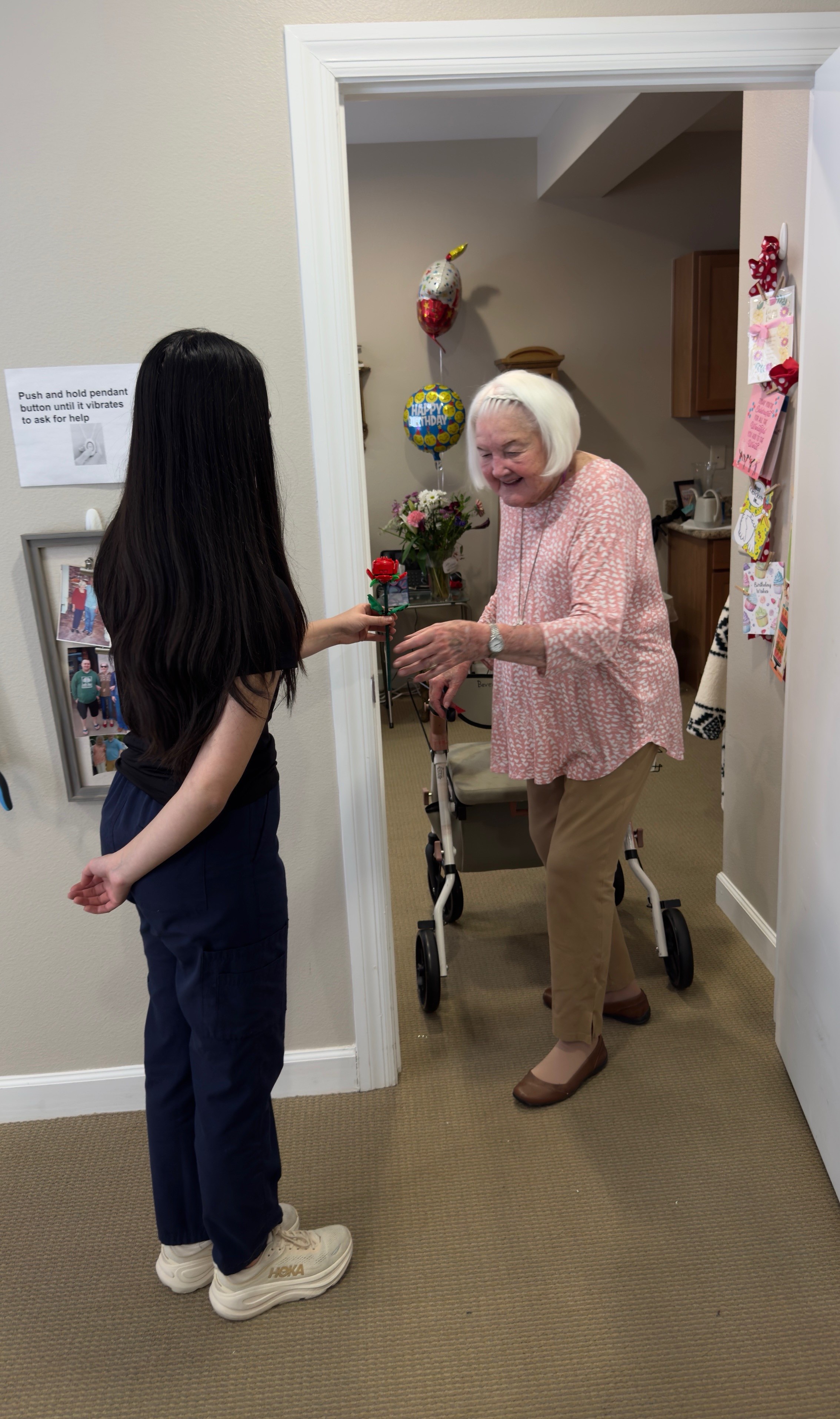 Photo of Alondra Trevizo, facing away from the camera, handing a senior living resident a rose.