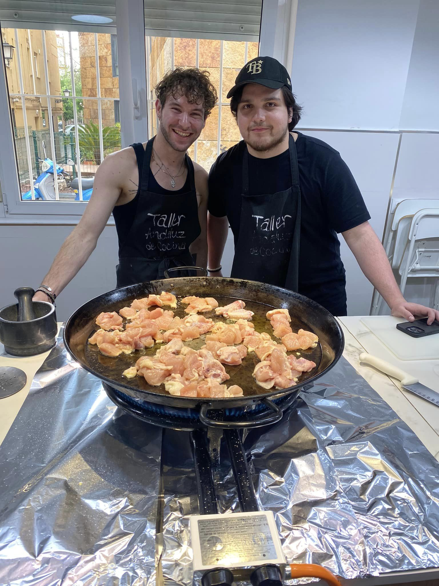 two young men cooking chicken on a large comal