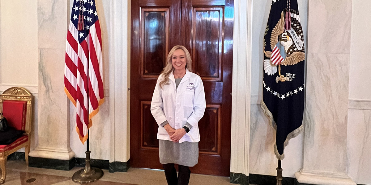 Vicki Brooks, in white medical coat, stands between two flags at the White House