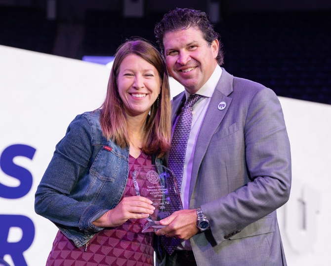 A smiling woman and man pose together onstage while holding a clear award recognizing Emily Lund, Ph.D., as Chancellor’s Distinguished Achievement Award recipient for Research and Creative Activity.